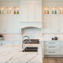 Bright and airy kitchen crafted by Nanaimo and Parksville kitchen designers at Classic Kitchens & Design, featuring a large white island with marble countertops and contrasting black cabinetry, lit by recessed lighting.