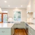 Two-tone traditional kitchen with a soft green island and lower cabinets, warm white upper cabinetry, farmhouse sink, stainless steel range, subway tile backsplash, and wood-framed patio doors.