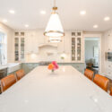 A kitchen renovation design in Nanaimo with white cabinets, stainless steel appliances, and a white marble island with brown stools. A pendant light hangs above and a vase with flowers adds a splash of color.