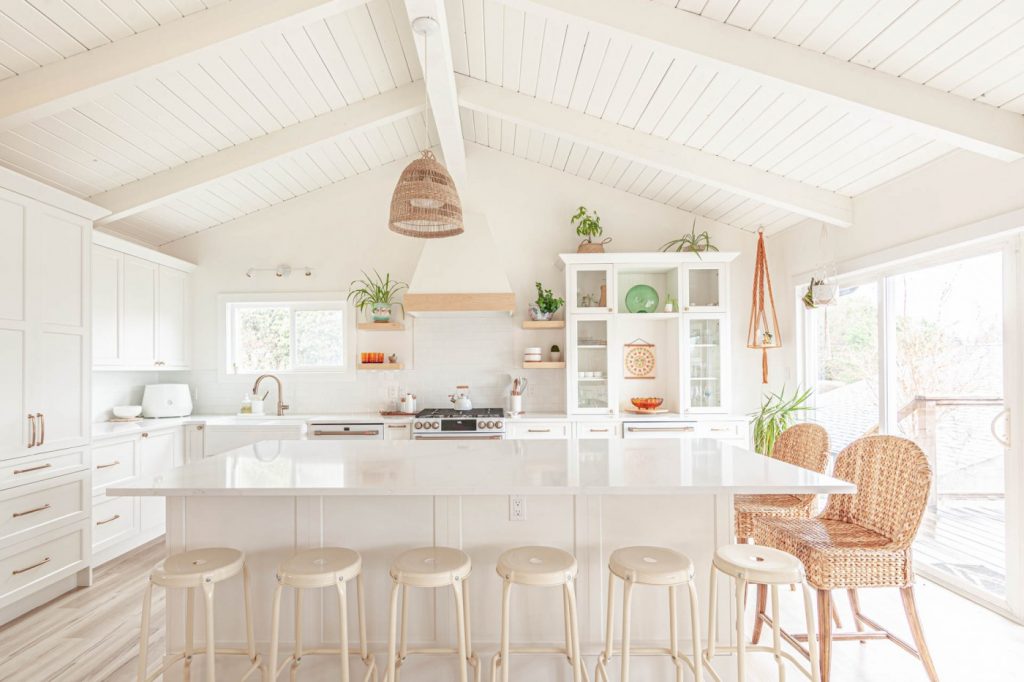 Large white kitchen island with multiple stools and end seating beneath a vaulted ceiling.