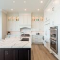 A modern kitchen featuring white shaker-style kitchen design cabinets with brushed nickel handles, complemented by a dark island base and marble countertops.