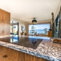 Mid-century modern kitchen island with dramatic Cambria Rose Bay quartz, built-in cooktop, walnut cabinetry, and large windows looking toward the water.