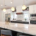 Townhouse kitchen design with Cambria Portrush quartz island, brass faucet and pendant lights, dark blue lower cabinets, white shaker cabinetry, and built-in wall appliances.