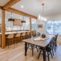 Open-concept modern country kitchen and dining area with Lectus Beckham two-tone maple cabinetry, large white quartz island, black pendant lights, exposed wood beams, and warm wood flooring