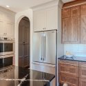 Custom kitchen cabinets in Nanaimo home featuring white upper cabinets, natural wood lower cabinets, black countertops, and stainless steel appliances.