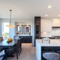 Open modern kitchen design and dining area with custom floating sideboard, large white island, high-gloss upper cabinets, dark wood cabinetry, built-in wine fridge, and bright window views