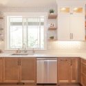 Two-tone kitchen white and wood kitchen cabinet design with warm lower drawers, tall painted upper cabinets, open shelving, stainless steel dishwasher, and under-cabinet lighting