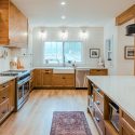 Two tone kitchen cabinets with warm wood lowers and crisp white uppers in a timeless mixed-material kitchen featuring a farmhouse sink, quartz countertops, and a custom wood hood.